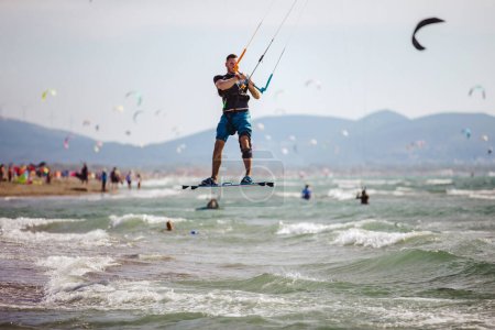 Foto de El kiter profesional hace el truco difícil. Un kiter macho cabalga sobre un hermoso fondo de olas y realiza todo tipo de maniobras. - Imagen libre de derechos