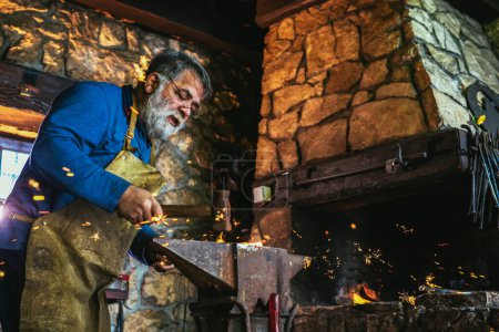 Foto de Herrero forjar manualmente el metal fundido en el yunque en la herrería con fuegos artificiales chispa - Imagen libre de derechos