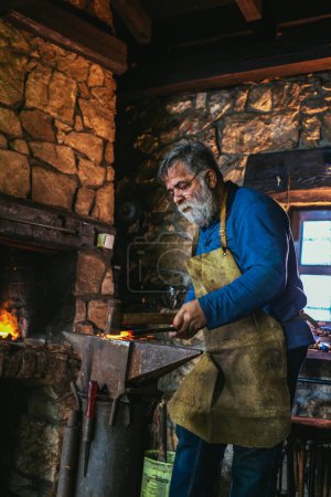 Photo for Blacksmith manually forging the molten metal on the anvil in smithy with spark fireworks - Royalty Free Image