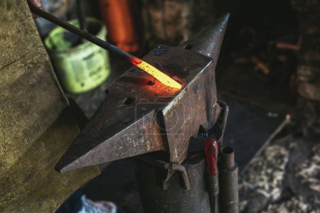 Photo for Blacksmith manually forging the molten metal on the anvil in smithy with spark fireworks, close up - Royalty Free Image