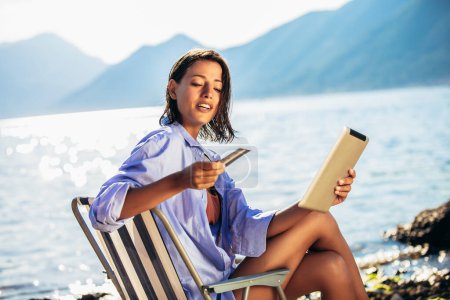 Téléchargez les photos : Femme heureuse avec tablette numérique et carte de crédit achetant en ligne assis près de la mer. - en image libre de droit