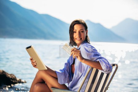 Photo for Happy woman with digital tablet and credit card buying online sitting near the sea. - Royalty Free Image