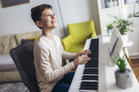 Téléchargez les photos : Petit garçon jouant du piano dans le salon. Enfant qui s'amuse à apprendre à jouer de l'instrument de musique à la maison. - en image libre de droit