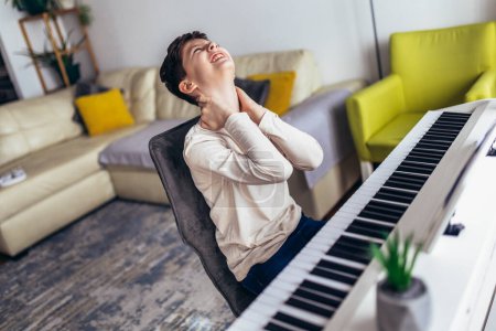 Photo for Little boy playing piano in living room. The boy is suffering from neck pain. - Royalty Free Image