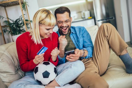 Téléchargez les photos : Jeune couple regardant un match de football sur tablette numérique et utilisant la carte de crédit pour les paris en ligne. - en image libre de droit