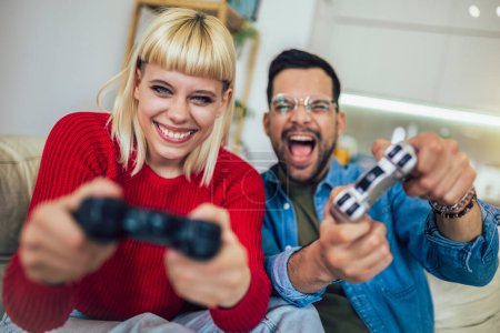 Foto de Novio y novia jugando videojuegos con joysticks en la sala de estar. Pareja cariñosa están jugando videojuegos en casa - Imagen libre de derechos