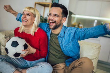 Téléchargez les photos : Jeune couple regardant un match de football à la télévision dans le confort de leur maison. - en image libre de droit