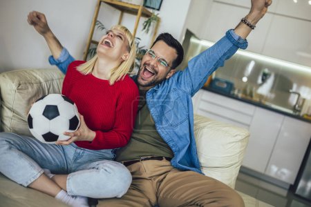 Photo for Young couple watching a football game on television from the comfort of their home. - Royalty Free Image