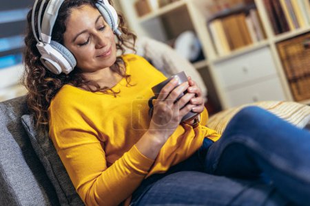 Téléchargez les photos : Femme portant un casque relaxant à la maison avec de la musique, profiter du temps libre. - en image libre de droit