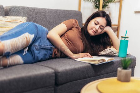 Photo for Teen girl lying on the couch and reads a book. Modern teenager at home. Teen literature concept. - Royalty Free Image