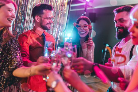 Gruppe von Freunden feiert in einem Nachtclub und prostet Drinks zu.