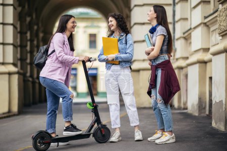 Téléchargez les photos : Étudiante en scooter rencontre avec ses camarades de classe sur le campus - en image libre de droit