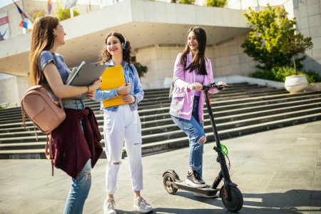 Téléchargez les photos : Étudiante en scooter étudier et parler avec ses camarades de classe - en image libre de droit