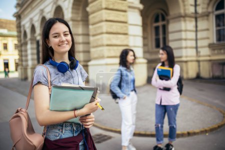 Photo for Student standing with her note-book while her friends are studying behind her - Royalty Free Image