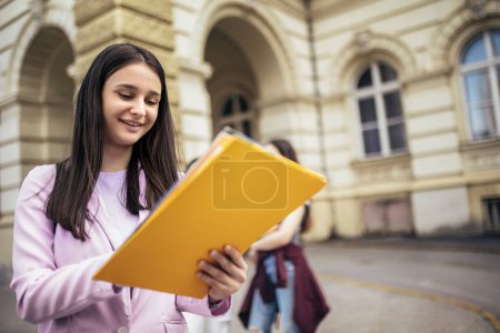 Téléchargez les photos : Étudiante debout avec son carnet de notes pendant que ses amis étudient derrière elle - en image libre de droit
