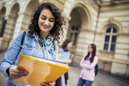 Téléchargez les photos : Étudiante debout avec son carnet de notes pendant que ses amis étudient derrière elle - en image libre de droit