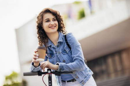 Photo for Student on scooter holding coffee outside on fresh air - Royalty Free Image