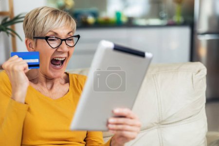 Téléchargez les photos : Sourire femme mûre shopping en ligne avec carte de crédit à l'aide d'une tablette numérique. - en image libre de droit