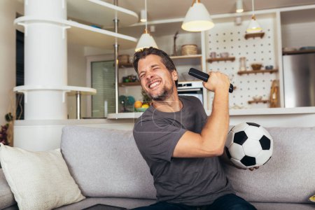 Téléchargez les photos : Jeune homme fan de football regardant le match de football à la télévision sur le canapé du salon. - en image libre de droit