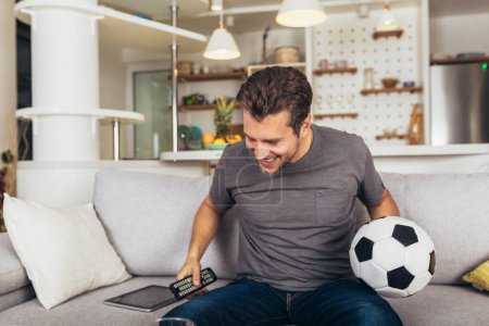 Téléchargez les photos : Jeune homme fan de football regardant le match de football à la télévision sur le canapé du salon. - en image libre de droit