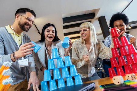 Photo for Group of young business people playing, building towers from plastic cups, two teams, blue and red. Teambuilding activity. - Royalty Free Image