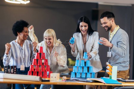 Foto de Grupo de jóvenes empresarios jugando, construyendo torres de vasos de plástico, dos equipos, azul y rojo. Actividad de Teambuilding. - Imagen libre de derechos