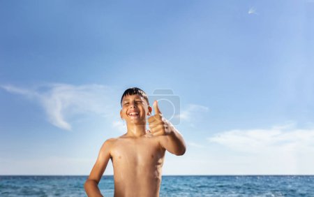 Foto de Un niño de nueve años es representado en la playa, completamente empapado. Su cabello castaño está mojado, pegado a su cara mientras gotas de agua gotean. - Imagen libre de derechos