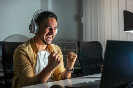 Foto de Un joven que trabaja hasta tarde en la oficina. Un hombre está sentado en una laptop en una oficina oscura - Imagen libre de derechos