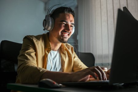 Foto de Un joven que trabaja hasta tarde en la oficina. Un hombre está sentado en una laptop en una oficina oscura - Imagen libre de derechos