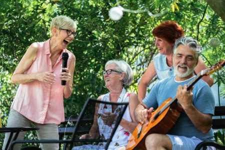 Foto de Grupo de personas mayores disfrutando de su retiro yendo de picnic, tocando una guitarra y cantando, haciendo barbacoa, haciendo recuerdos y fortaleciendo su amistad - Imagen libre de derechos