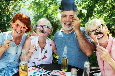 Photo for Elderly people are making themselves young again and coming out of their comfort zone using silly glasses, hats, and mustaches.They are also drinking their favourite beverages and making great memories - Royalty Free Image