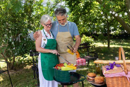 Photo for Elderly couple celebrate the 4th of July in their backyard. They are making barbeque, vegetables, and drinking beverages while enjoying and making memories - Royalty Free Image