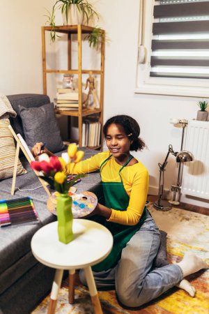 Téléchargez les photos : Une préadolescente utilise un pinceau pour donner vie à la créativité et à la couleur sur une table, créant un chef-d'œuvre de fleurs d'intérieur. - en image libre de droit