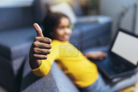 Photo for Smiling school African American girl holding thumbs up, homeschooling concept - Royalty Free Image
