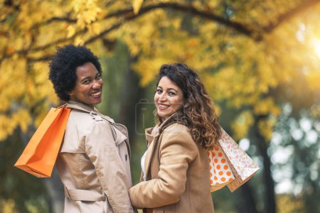 Téléchargez les photos : Amies heureuses marchant dans la forêt en automne avec des sacs à provisions. - en image libre de droit