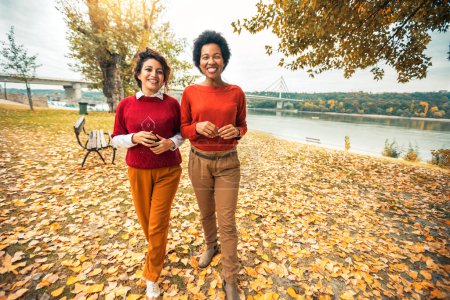 Téléchargez les photos : Deux jeunes femmes souriantes amies jogging dehors dans la forêt à côté du lac en sweat-shirts rouges - en image libre de droit