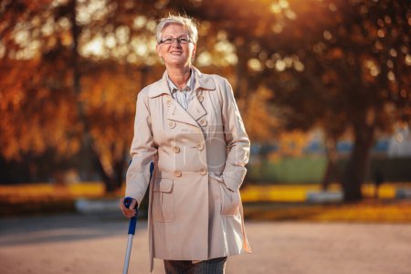 Téléchargez les photos : Une femme heureuse plus âgée marche avec une canne dans le parc coloré à l'automne - en image libre de droit