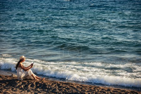 Téléchargez les photos : Adolescente utilisant une tablette numérique pour prendre des photos sur la plage - en image libre de droit