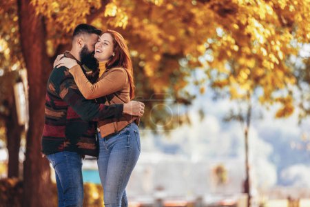 Foto de Joven pareja feliz mirándose mientras se toman de la mano y caminan en el parque de otoño. - Imagen libre de derechos