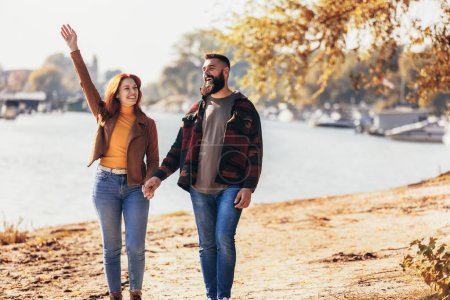 Photo for Happy young couple in love holding hands and walking on coast near river. - Royalty Free Image
