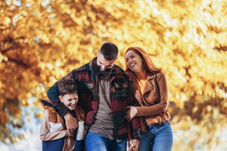 Téléchargez les photos : Jeunes parents heureux s'amuser avec leur garçon tout en courant dans le parc pendant la journée d'automne. - en image libre de droit