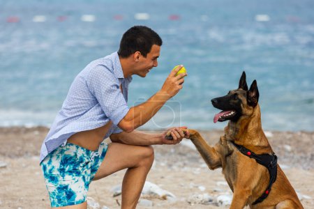 Téléchargez les photos : Un dresseur de chien avec un chien pendant l'entraînement près de la mer - en image libre de droit