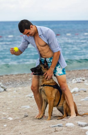 Foto de Un entrenador de perros con un perro durante el entrenamiento cerca del mar - Imagen libre de derechos
