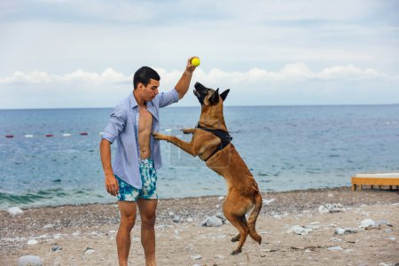Foto de Un entrenador de perros con un perro durante el entrenamiento cerca del mar - Imagen libre de derechos
