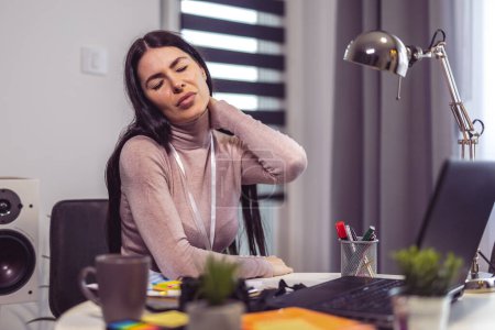 Foto de Joven mujer frustrada que trabaja en el escritorio de la oficina que sufre de dolores de cabeza diarios crónicos - Imagen libre de derechos