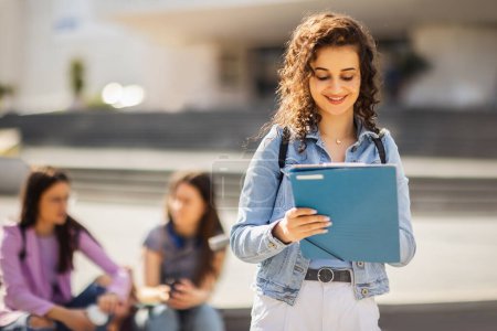 Photo for Student standing with her note-book while her friends are studying behind her - Royalty Free Image