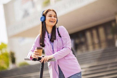 Téléchargez les photos : Étudiant en scooter tenant le café à l'extérieur sur l'air frais - en image libre de droit