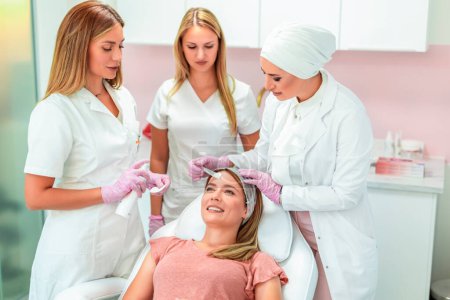 Photo for Three beautiful doctors and cosmeticians doing multiple facial treatments on a young  woman's face - Royalty Free Image