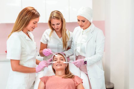 Photo for Three beautiful doctors and cosmeticians doing multiple facial treatments on a young  woman's face - Royalty Free Image