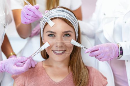 Foto de Tres médicos y cosméticos haciendo múltiples tratamientos faciales en la cara de una mujer joven - Imagen libre de derechos